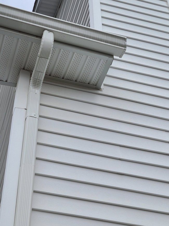 Seamless gutter downspout installed and fastened along the side of a house